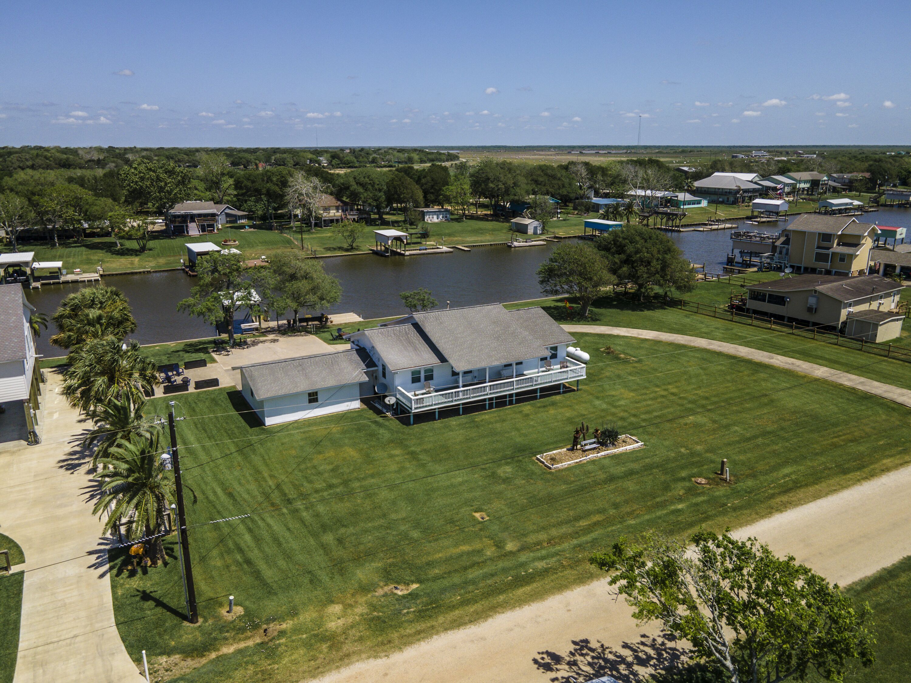 An aerial view of a residential area with a large house featuring a balcony, a dock, and a lake in the background.