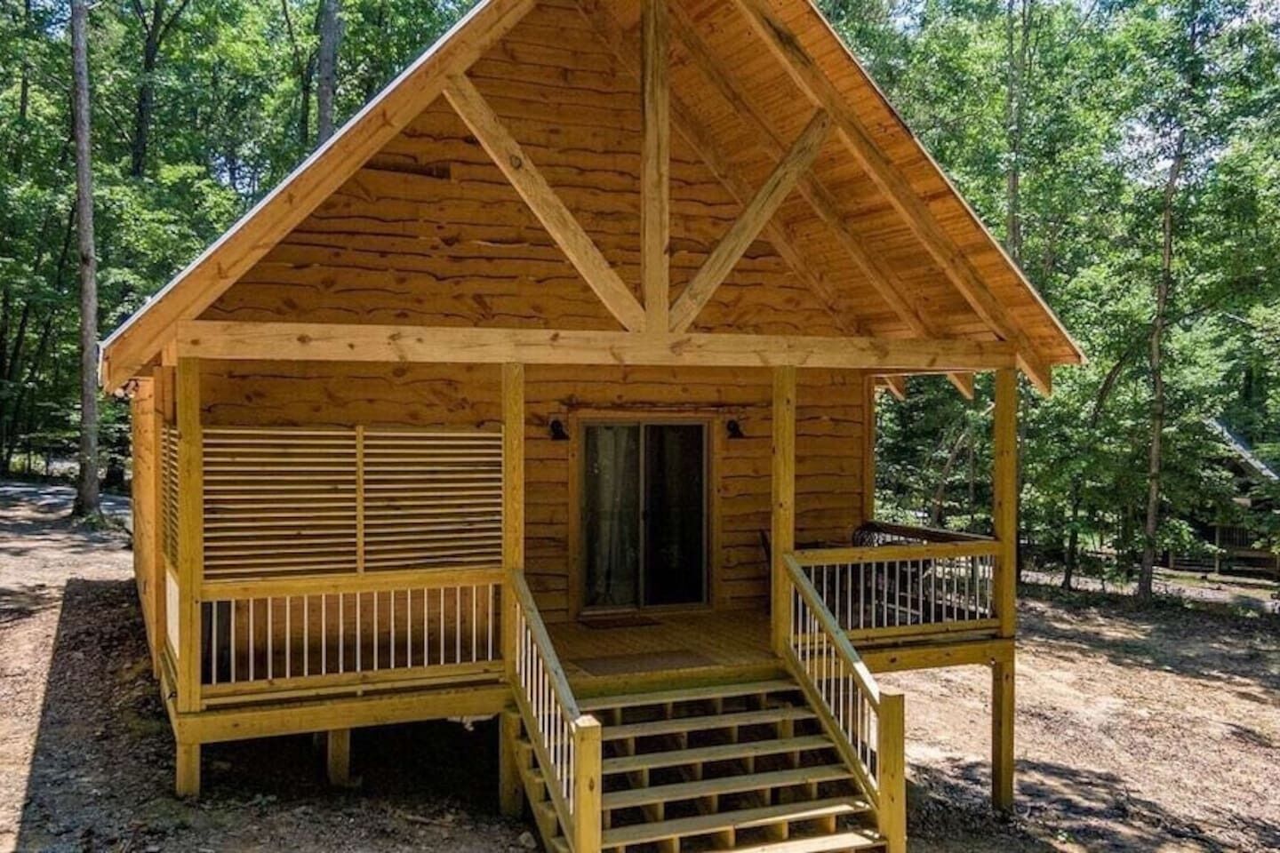 Una cabaña de madera con techo inclinado, un porche con barandillas y una puerta.