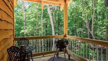 Um deck de madeira com mesa, cadeiras, churrasqueira e vista para uma floresta.