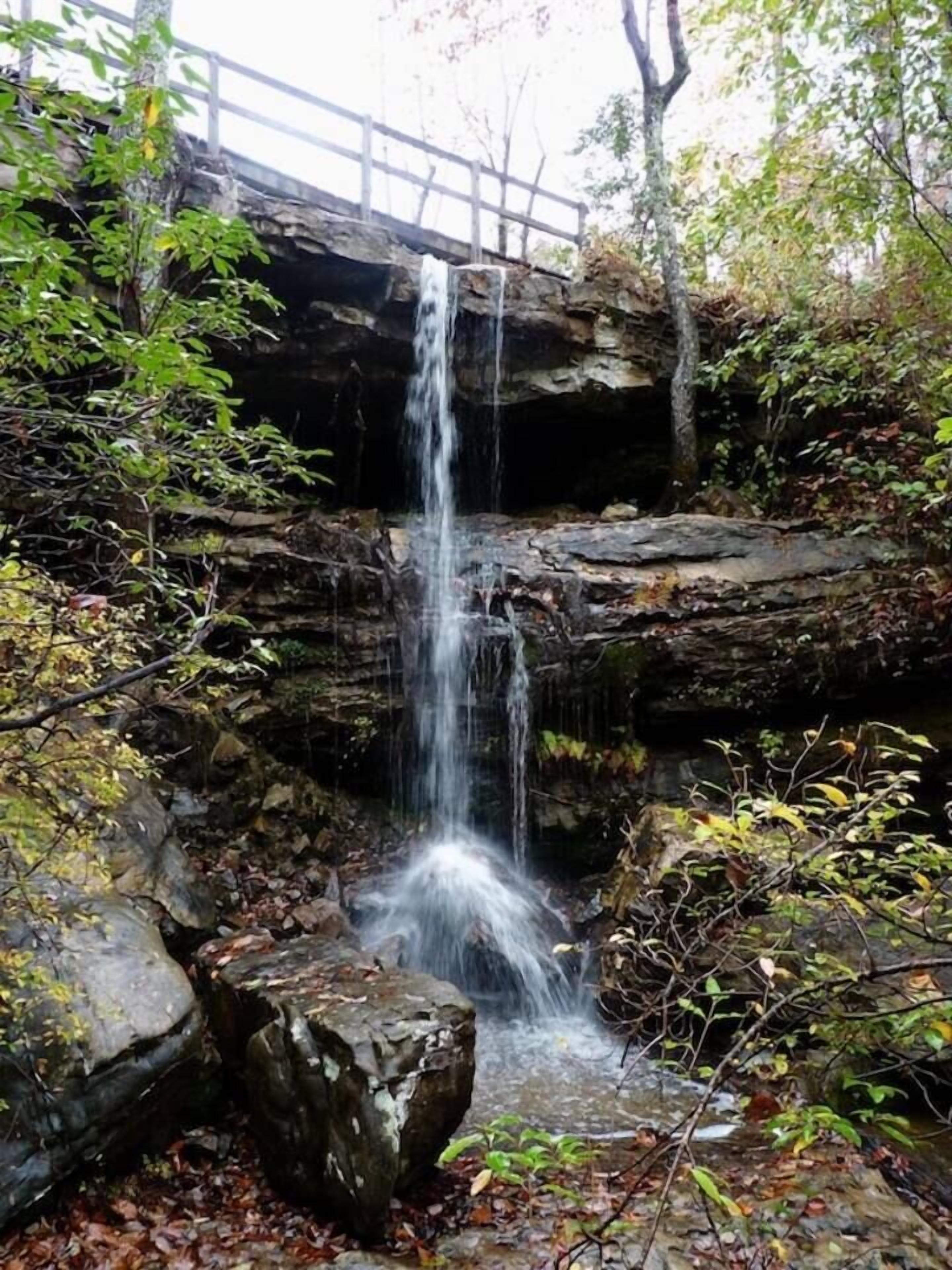 Een waterval die over een rotswand stroomt, met een houten brug erboven.