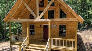 A wooden cabin with a front porch, a red door, and a sign that reads "Cottage." - Quail's Nest with Hot tub (Mentone)