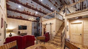A rustic interior with a wooden staircase, a red leather sofa, a wooden dining table, and a chandelier. - Quail's Nest with Hot tub (Mentone)