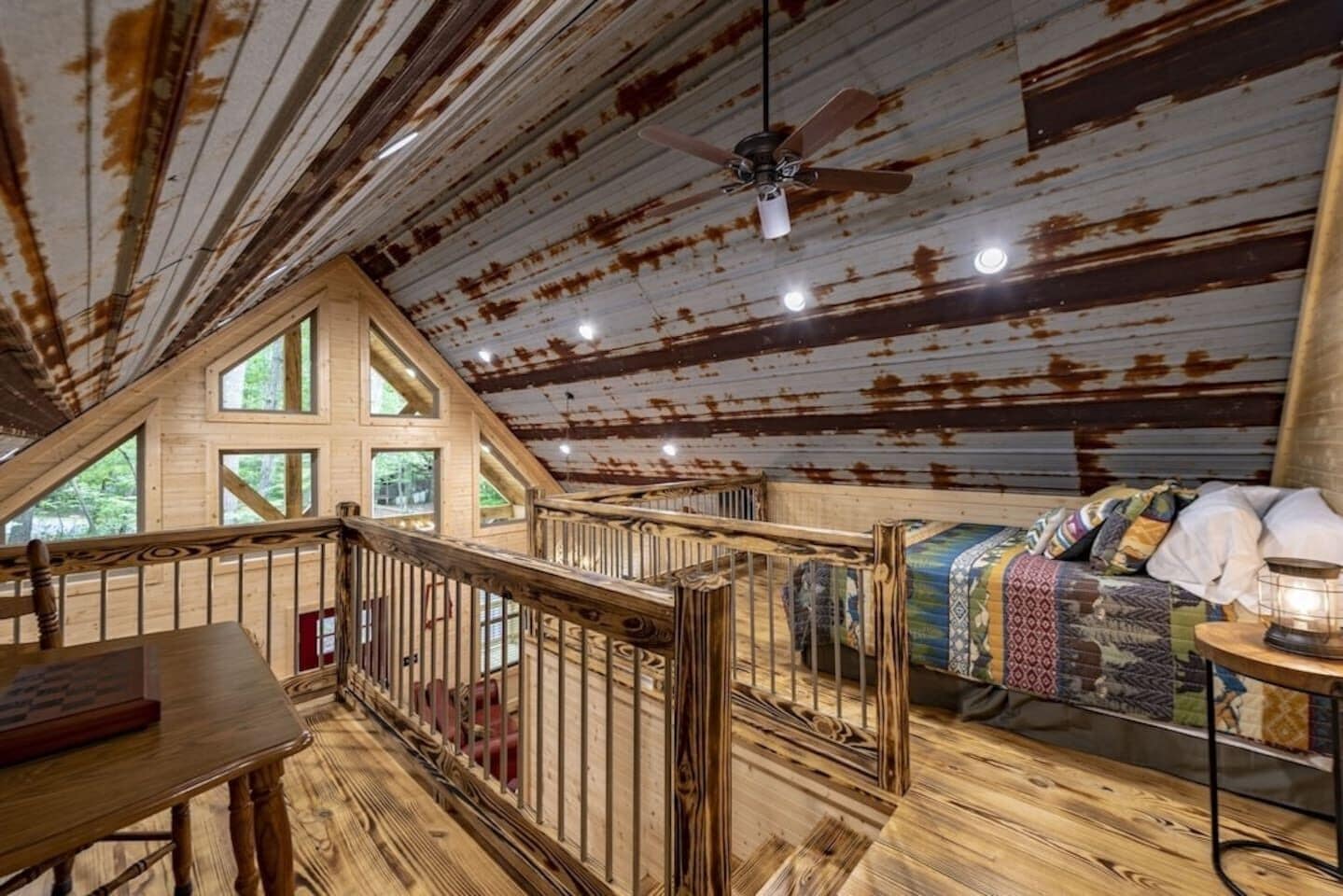 Interior rústico de una cabaña con un dormitorio en entrepiso, pisos de madera y un balcón con barandilla.