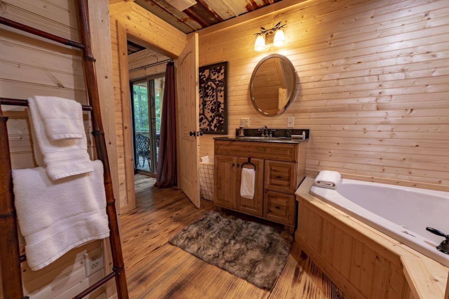 Ein Badezimmer einer Holzhütte mit Holzboden, einem großen Spiegel, einer Badewanne und einem hölzernen Waschtisch.