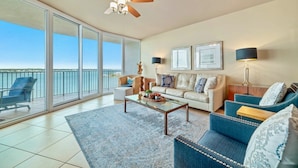 A spacious living room with a large glass door leading to a balcony, a ceiling fan, a coffee table, and a sofa set. - Caribe Resort D606 | Exquisite Bay Front Condo, Endless Amenities! (Orange Beach)