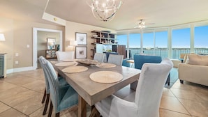 A spacious dining area with a large table, chairs, and a chandelier. There is a balcony with a view of the water. - Caribe Resort D606 | Exquisite Bay Front Condo, Endless Amenities! (Orange Beach)