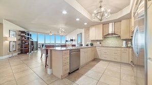 A spacious kitchen with a central island, light wood cabinetry, and a modern chandelier. - Caribe Resort D606 | Exquisite Bay Front Condo, Endless Amenities! (Orange Beach)