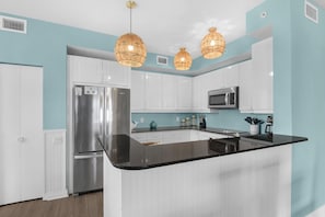 A modern kitchen with white cabinets, a stainless steel refrigerator, a microwave, and a black countertop island. - Beach Colony West 16F- 3BR Gulf Front w/Beach Service and Onsite Management (Navarre)