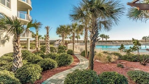 A pathway leading to a pool area with palm trees and a building with balconies. - Beach Colony West 16F- 3BR Gulf Front w/Beach Service and Onsite Management (Navarre)