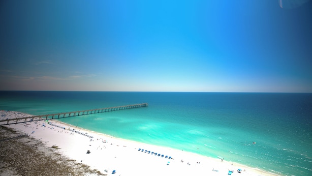 A beach with a pier extending into the ocean, sandy beach, and clear turquoise water. - Beach Colony West 16F- 3BR Gulf Front w/Beach Service and Onsite Management (Navarre)