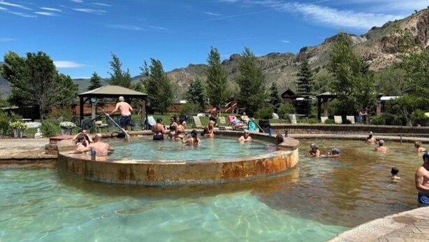 Una piscina con gente alrededor, rodeada de árboles y montañas.