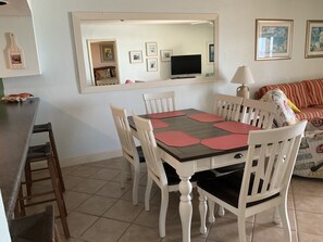 Un comedor con una mesa rectangular, seis sillas, un televisor sobre un mueble bajo y un sofá al fondo.