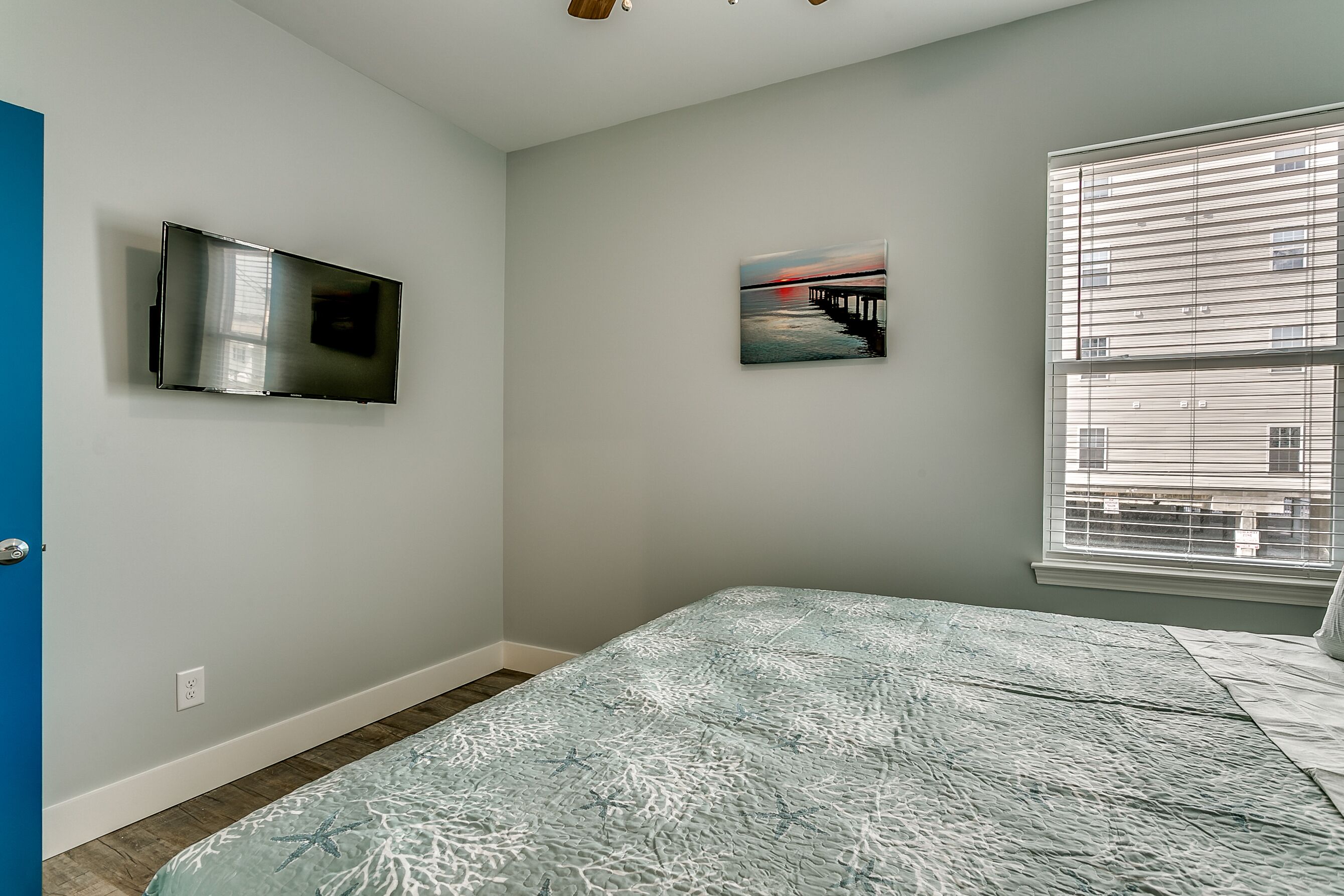 A bedroom with a bed, a TV mounted on the wall, and a window with blinds.