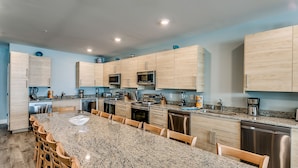 Una cocina moderna con encimeras de granito, armarios de madera, electrodomésticos de acero inoxidable y una isla grande con asientos.