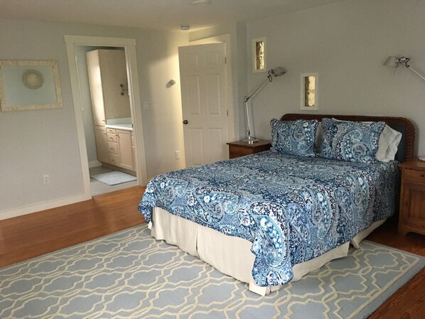 A bedroom with a bed, bedside lamps, a nightstand, a patterned rug, and a door leading to a bathroom. - SUNNY second floor 2BD, 2BT  (Nantucket)