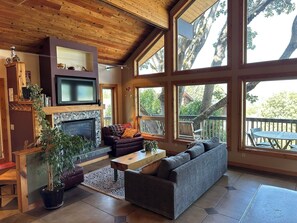A cozy living room with a fireplace, comfortable seating, and large windows offering a view of the outdoors. - Columbia Tree House - Downtown Hood River with Big View and Fenced Yard (Hood River)