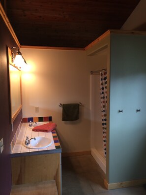 Un baño con techo de madera, lavamanos, espejo, toallero y cortina de ducha.