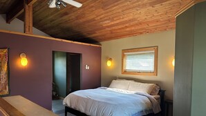 Ein Schlafzimmer mit Holzbalkendecke, einem Bett mit weißer Bettwäsche, einer Bank und zwei Wandleuchten.