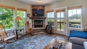 A living room with a fireplace, a television, and large windows offering a view of the outdoors. -  Luxury Riverwalk Townhome Overlooking The River, Hot Tub, A/C, Close To Town. (Pagosa Springs)