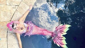 Una persona vestida con un traje de sirena rosa está de pie al borde de una piscina.