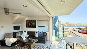 Ein modernes Wohnzimmer mit Sofa, Couchtisch und Kunstwerken mit Blick auf eine Stadtlandschaft und einen Strand.