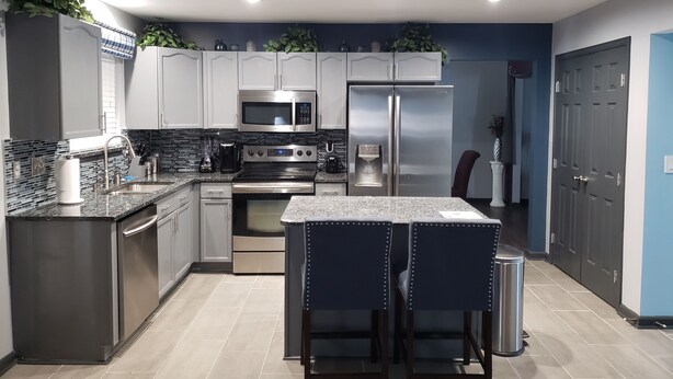 A modern kitchen with stainless steel appliances, a double sink, and a bar area with stools. - Uptown Charlotte, Airport, National White Water Center, Other Major Attraction (Charlotte)