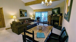 A cozy living room with a sofa, dining table, chairs, a fireplace, and a television. - Remodeled Condo w/ FREE WiFi, Parking, Heated Pool, Hot Tubs, Skier Shuttles (Avon)