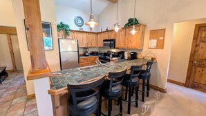 A kitchen with wooden cabinets, a refrigerator, a microwave, a stove, and bar stools. - Remodeled Condo w/ FREE WiFi, Parking, Heated Pool, Hot Tubs, Skier Shuttles (Avon)