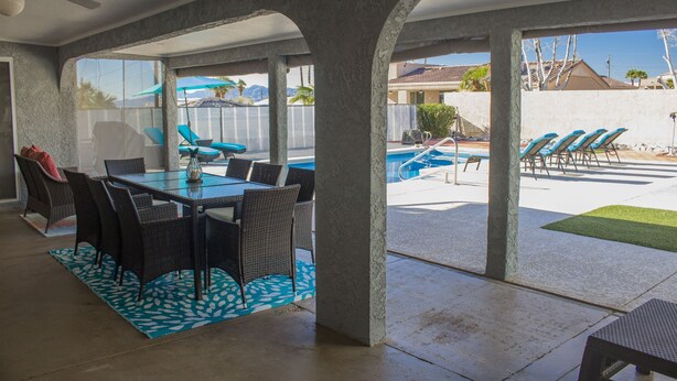 Ein überdachter Patio-Bereich mit Esstisch und Stühlen, einem Pool und Liegestühlen.