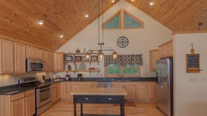 A spacious kitchen with wooden cabinets, a central island, stainless steel appliances, and a large window. - Get-Away Mountain Cabin. Hot Tub, Sunset Mtn. Views, Game Room, Near Asheville (Mars Hill)