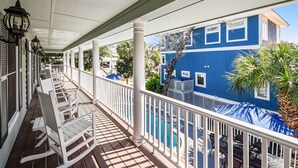 Ein überdachter Balkon mit weißen Geländern und Schaukelstühlen, der auf ein blaues Gebäude mit Pool blickt.