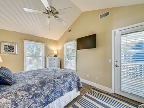 A bedroom with a bed, a ceiling fan, a TV mounted on the wall, and a door with blinds.