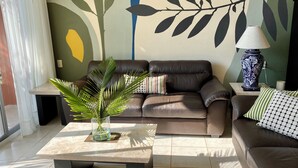 A living room with a brown leather sofa, a glass coffee table with a plant, and a decorative lamp.
