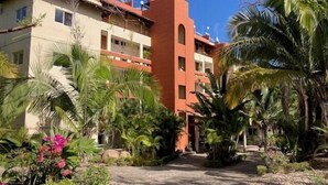 A building with multiple balconies, surrounded by tropical vegetation and a paved pathway.