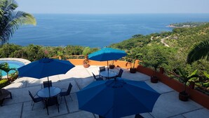 A patio with outdoor seating and umbrellas overlooking a scenic ocean view.