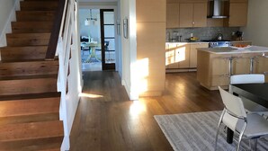 Eine moderne Küche mit Holzboden, eine Essecke mit weißem Tisch und Stühlen sowie eine Treppe mit Holzstufen.