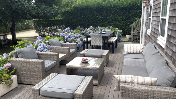 Eine Terrasse mit Korbmöbeln, darunter Sofas und ein Tisch, umgeben von Hortensienblüten.