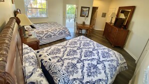A bedroom with two beds, a ceiling fan, a dining table with chairs, and a dresser.