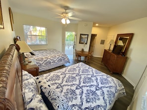A bedroom with two beds, a ceiling fan, a dining table with chairs, and a dresser.