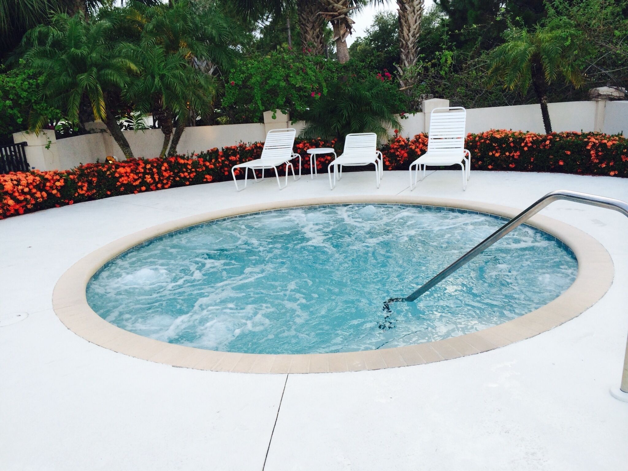 Un jacuzzi rodeado de sillones blancos y flores rojas.