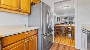 A kitchen with wooden cabinets, a stainless steel refrigerator, and a dining area with a wooden table and chairs. - Nye Beach, Restaurants, Shop! Walk to the Beach! (Newport)