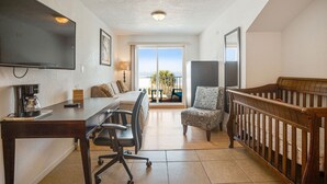 A room with a desk, chair, crib, and a TV.