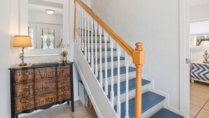 A staircase with white railings and blue steps, a wooden console table with decorative items, and a mirror above the console.