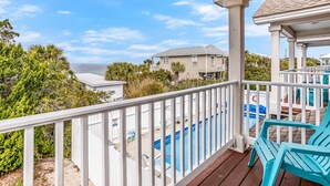 A wooden deck with a pool, white railings, and a view of the ocean.