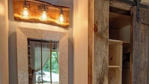 A rustic bathroom with a wooden vanity, a mirror with a wooden frame, and a shelf with a vase.