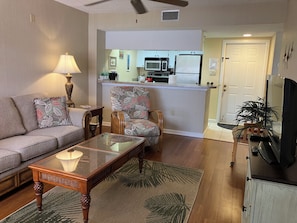 A living room with a sofa, a glass-top coffee table, a patterned armchair, and a television.