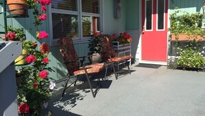 A porch with a red door, a white-framed window, and a chair with a floral cushion. - Spacious and conveniently located duplex (Anchorage)