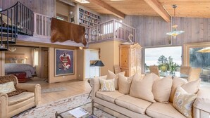 A spacious living room with a high ceiling, a large leather sofa, a glass coffee table, and a balcony with a wooden railing. - Come take in the ocean, gaze at the starry skies, commune with nature. (The Sea Ranch)