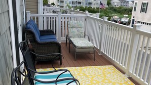 A balcony with two wicker chairs and a lounge chair, a yellow patterned rug, and a view of neighboring houses. - Gorgeous Seaside Village On Golf Course Rd In Sought After West OC (Ocean City)