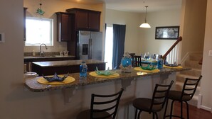 A kitchen with a central island, bar stools, a refrigerator, and a dining area with chairs and a table. - Gorgeous Seaside Village On Golf Course Rd In Sought After West OC (Ocean City)